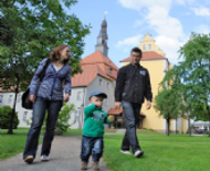 Eine Familie geht auf der Schlossinsel spazieren, dahinter das Lübbener Schloss