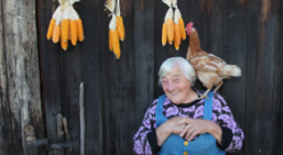 Bäuerin auf ihrem Hof Ältere Frau mit Huhn auf der Schulter, im Hintergrund Maiskolben an der Scheuenwand