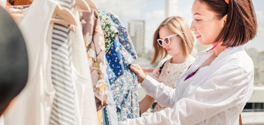 Two happy girls friends choosing and shopping fot clothes in boutique or outdoor flea market